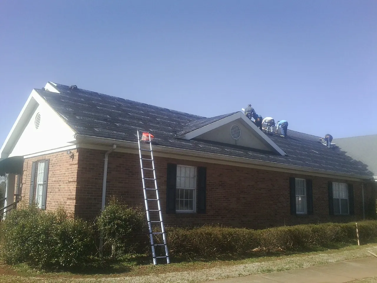 Crew tearing shingles off a brick ranch roof with a ladder set — Emergency Roof Repair work by our crew in Gloucester