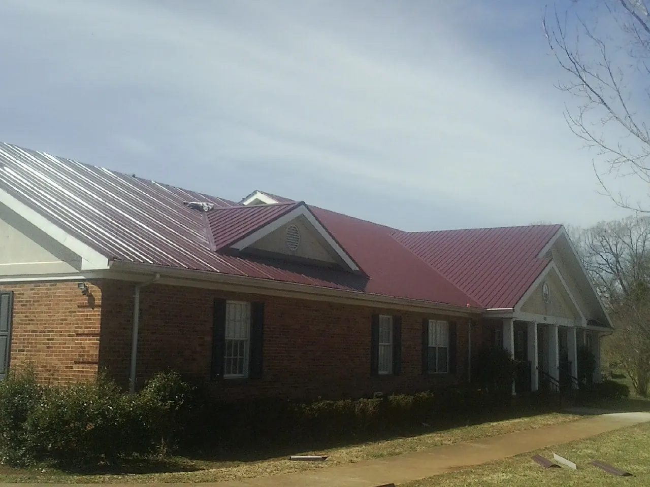 Red metal roof with gabled entries on a long brick building, from a Hail Damage Roof Repair job in Gloucester