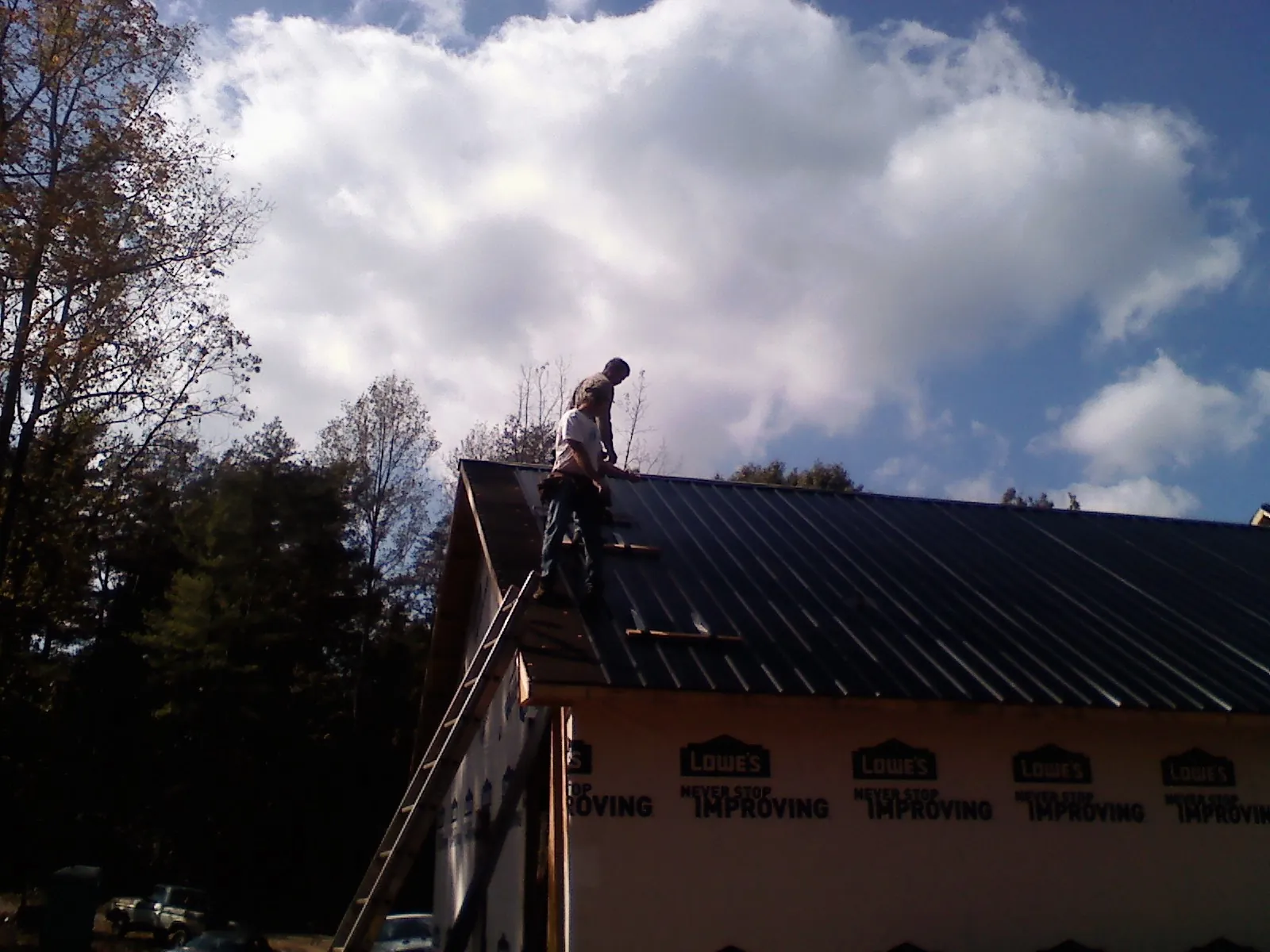 Roofer fastening dark metal panels high against a cloudy sky, from a Roof Inspection job in Gloucester