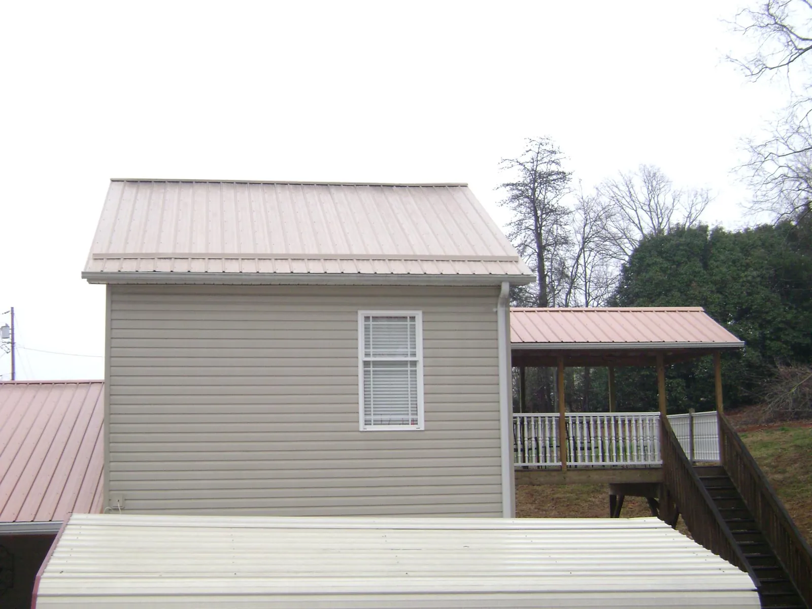 Tan metal roofs on a two story addition and attached porch, from a Roof Replacement job in Gloucester